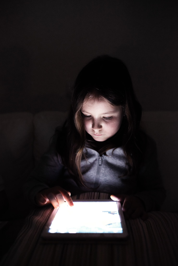 暗闇の中に座って、タブレットで遊ぶ小さな女の子 - 写真・画像