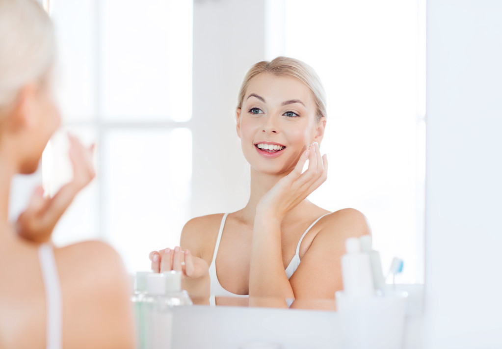 mujer feliz aplicando crema a la cara en el baño
 - Foto, Imagen