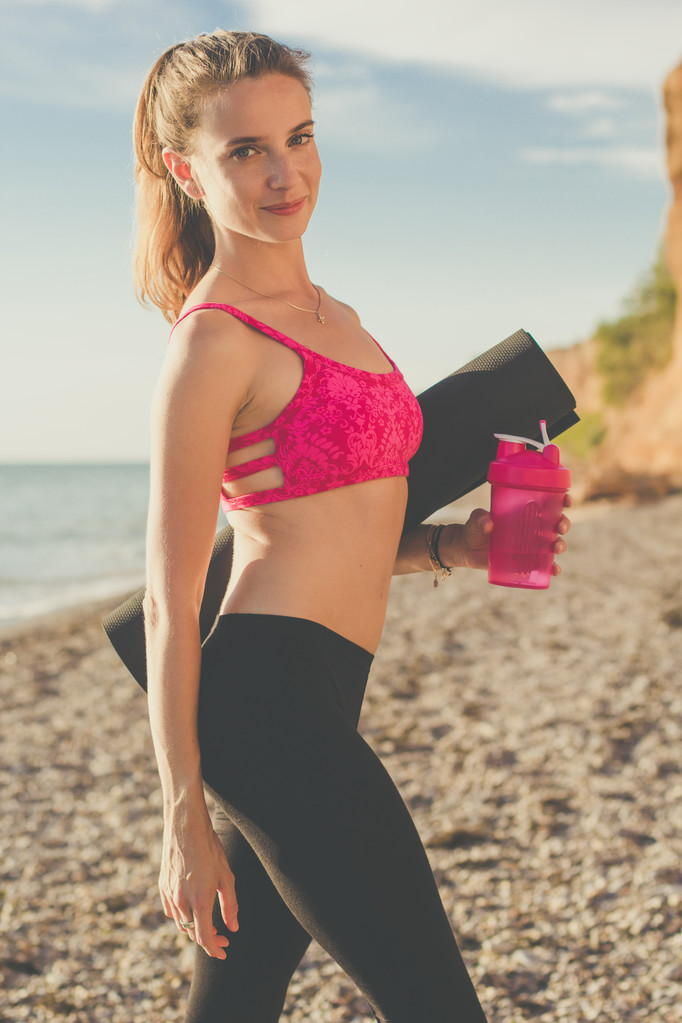 Femme sportive avec bouteille et tapis sur la plage
 - Photo, image