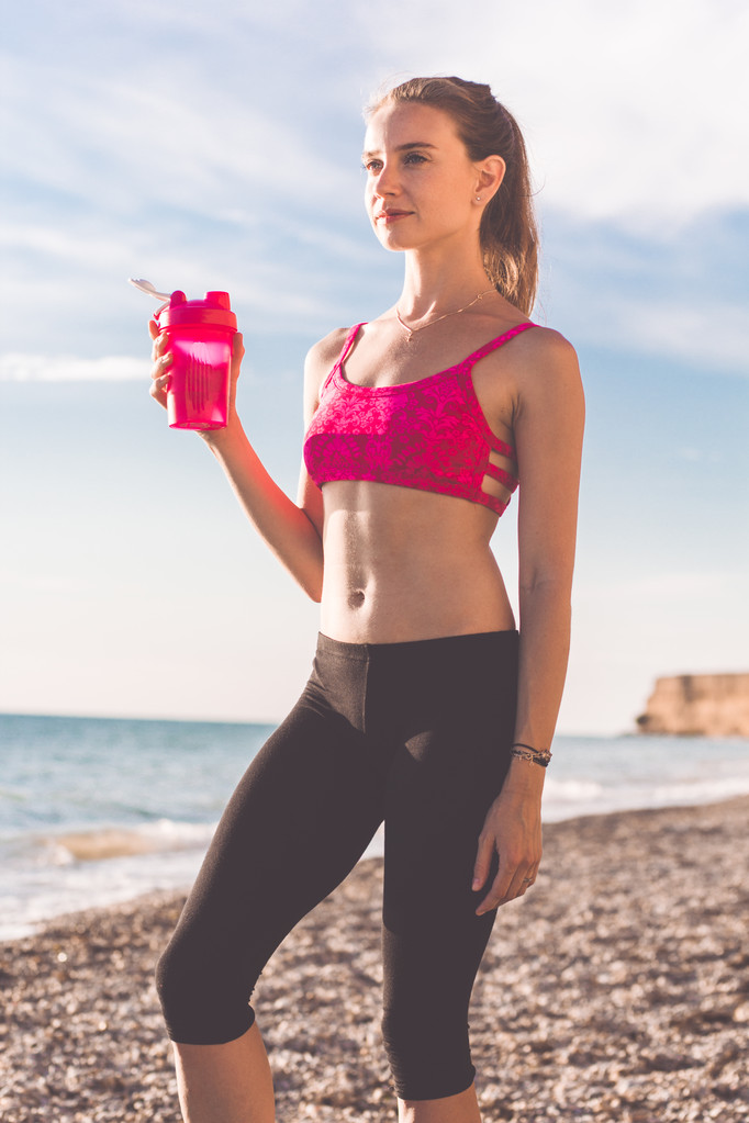 Fiatal nő, rózsaszín üveg a strandon - Fotó, kép