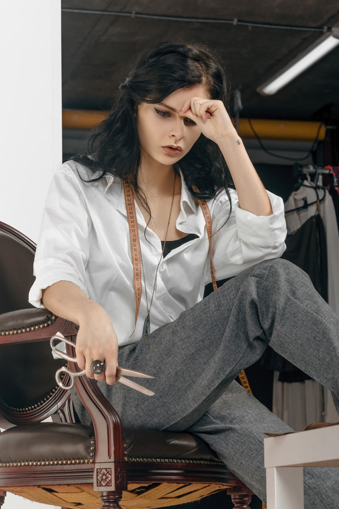 Σχεδιαστής μόδας κάθεται με ψαλίδι στο χέρι της. - Φωτογραφία, εικόνα