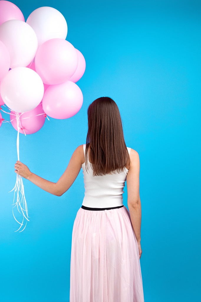 Вид ззаду на невпізнавану дівчину в спідниці з багатьма рожевими повітряними кулями на синьому фоні. Студійний знімок
 - Фото, зображення