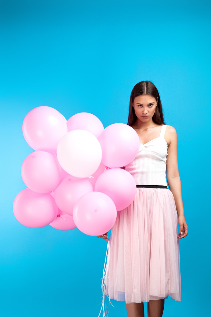 Portrét bruneta s klidnou tváří při pohledu na fotoaparát s růžové bubliny na modrém pozadí - Fotografie, Obrázek