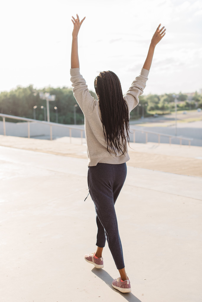Vista lateral trasera de la mujer feliz con auriculares y manos levantadas caminando al aire libre en tiempo soleado
 - Foto, imagen