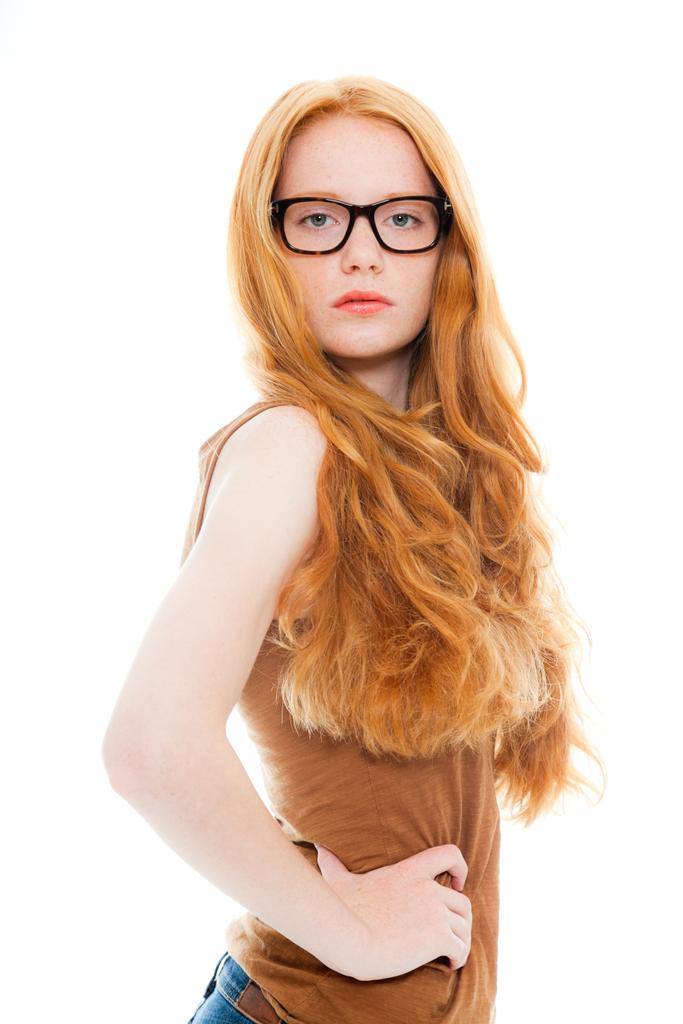 Chica bonita con el pelo largo y rojo con camisa marrón y gafas vintage. Estudio de moda tiro aislado sobre fondo blanco
. - Foto, imagen