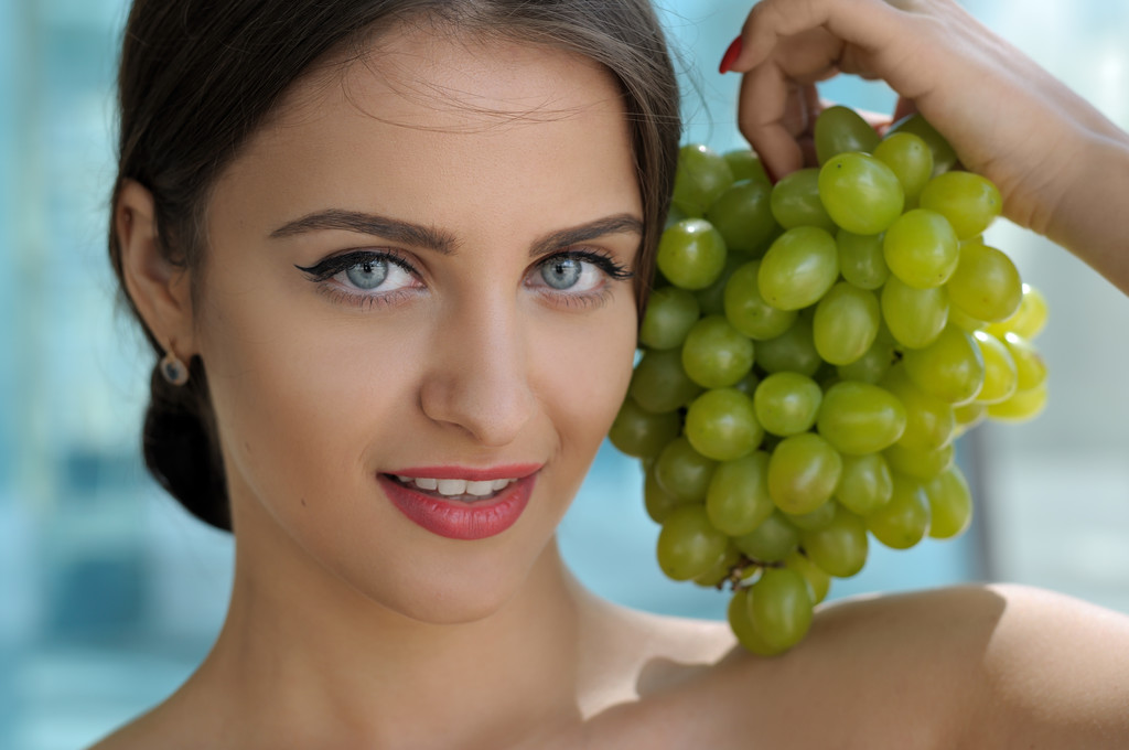 Kobieta stwarzających z kiści winogron i uśmiechając się. - Zdjęcie, obraz