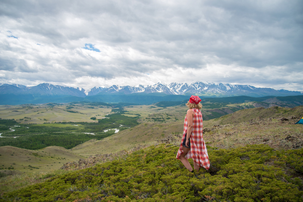 nainen seisoo nurmikolla ja katselee vuoria
 - Valokuva, kuva