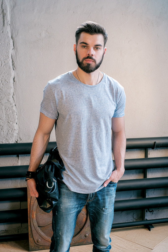 Portrait of calm bearded good-looking man with handbag looking at camera.Old wall on background. - Photo, Image