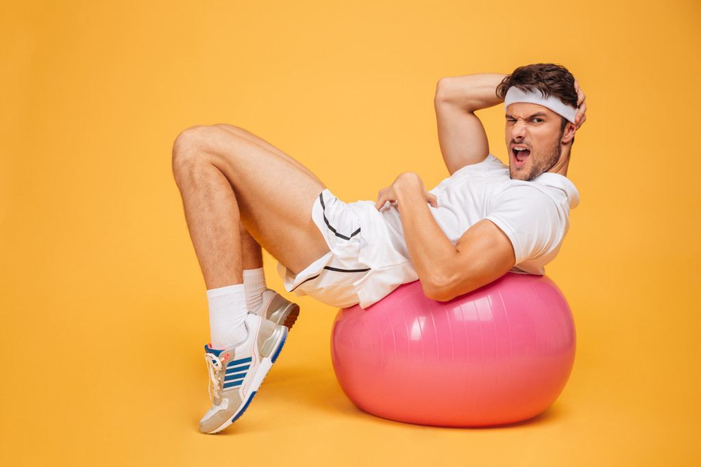 Sportman abs op fitness bal doen over oranje achtergrond - Foto, afbeelding