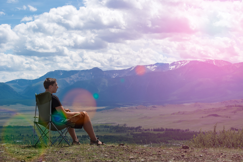 mies istuu tuolilla vuorilla ja katsoo kaukaisuuteen
 - Valokuva, kuva