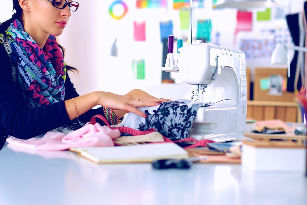 Jovem mulher costura enquanto sentado em seu local de trabalho - Foto, Imagem