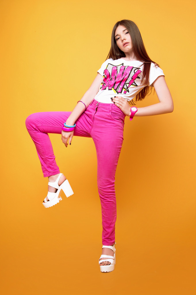 Een mooie 13-jarige meisje gekleed in roze broek en een T-shirt in Studio op gele achtergrond - Foto, afbeelding