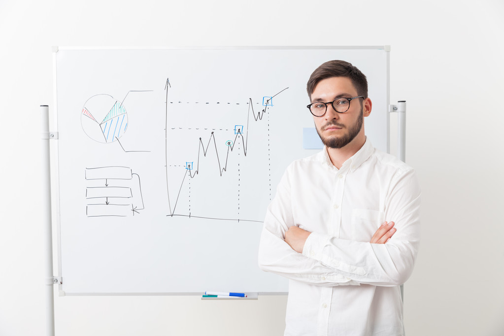 Businessman in glasses with beard is standing near whiteboard with diagrams, his hands crossed. Looking to camera  - Photo, Image