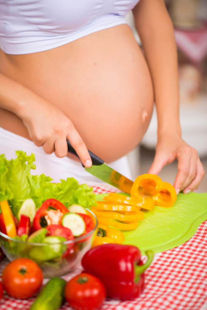 Primer plano de una barriga embarazada. Mujer embarazada en la cocina preparando una ensalada de verduras
. - Foto, imagen