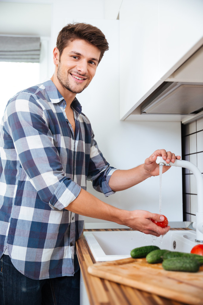 Ayakta ve yıkama sebze mutfak mutlu genç adam - Fotoğraf, Görsel