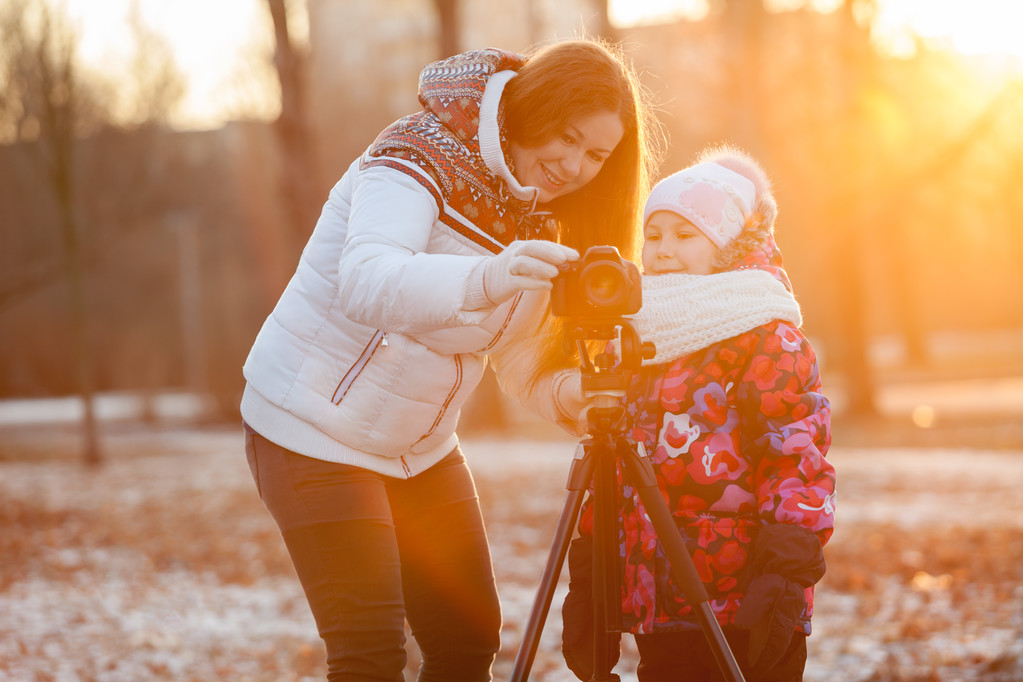 Mutter und Kind stellen die Kamera auf Stativ in den Strahlen der untergehenden Sonne auf - Foto, Bild