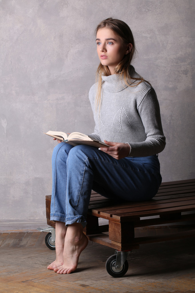 Tyttö villapaidassa pitelee kirjaa. Harmaa tausta
 - Valokuva, kuva