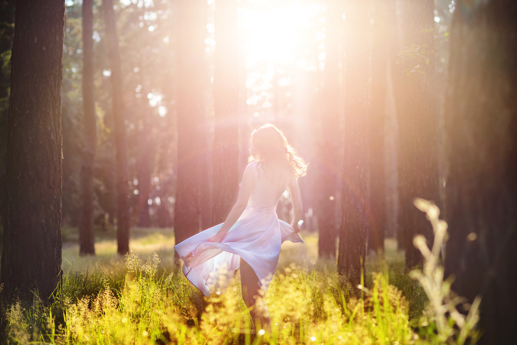 木 々の葉を通して日光の光線を持つフォレストのエレガントな光の青いドレスに立って身に着けている美しい若い女性。ソフト フォーカスとある調子を与える - 写真・画像