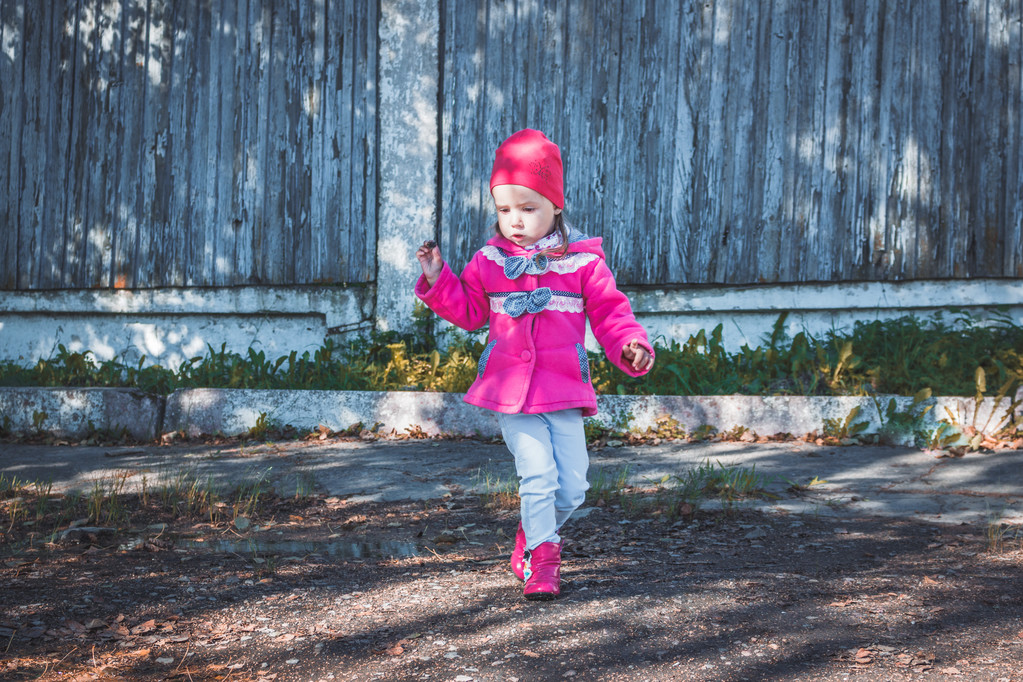 Маленька дівчинка в рожевому пальто, джинси і чоботи, що йдуть парком
 - Фото, зображення