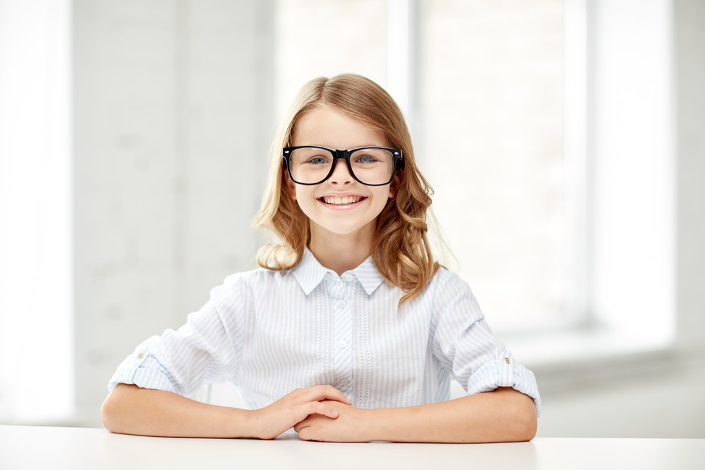 щаслива школярка в окулярах, сидячи за столом
 - Фото, зображення