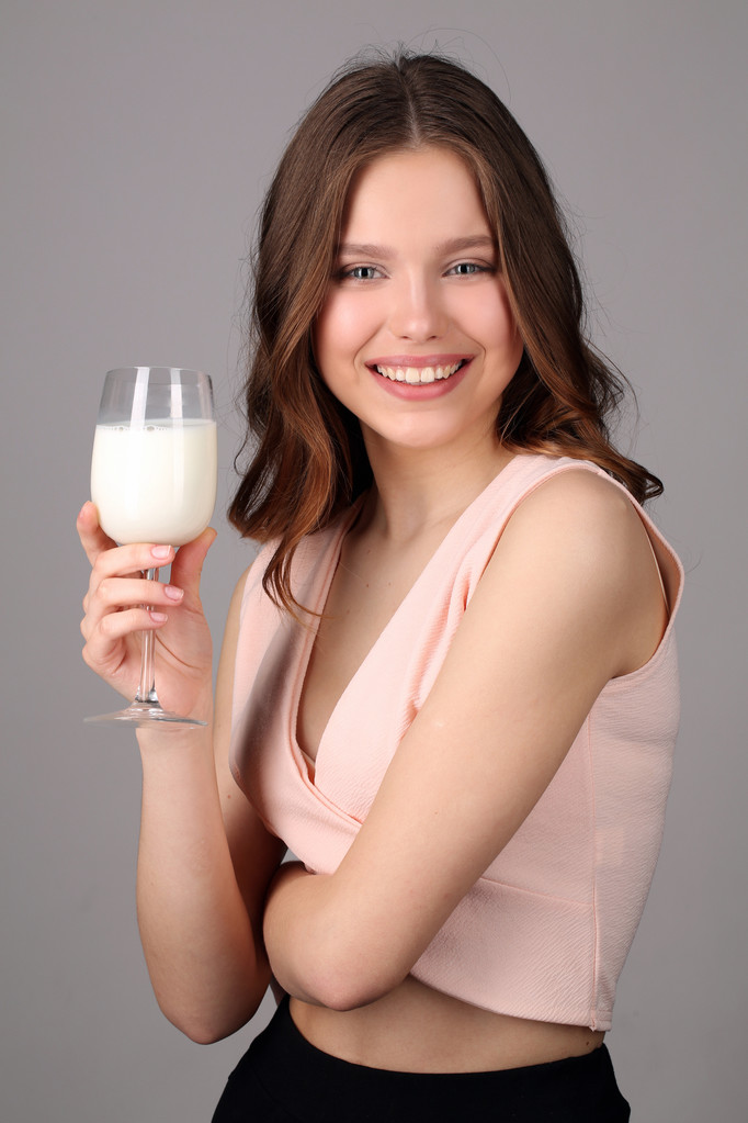 Mädchen posiert mit einem Glas Milch. Nahaufnahme. grauer Hintergrund - Foto, Bild