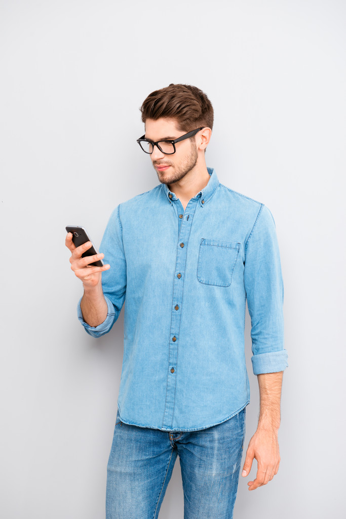 Retrato de jovem homem inteligente em óculos leitura sms no celular ph
 - Foto, Imagem