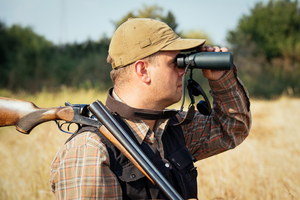 Uomo cacciatore con fucile guardando attraverso binocoli nella foresta
 - Foto, immagini