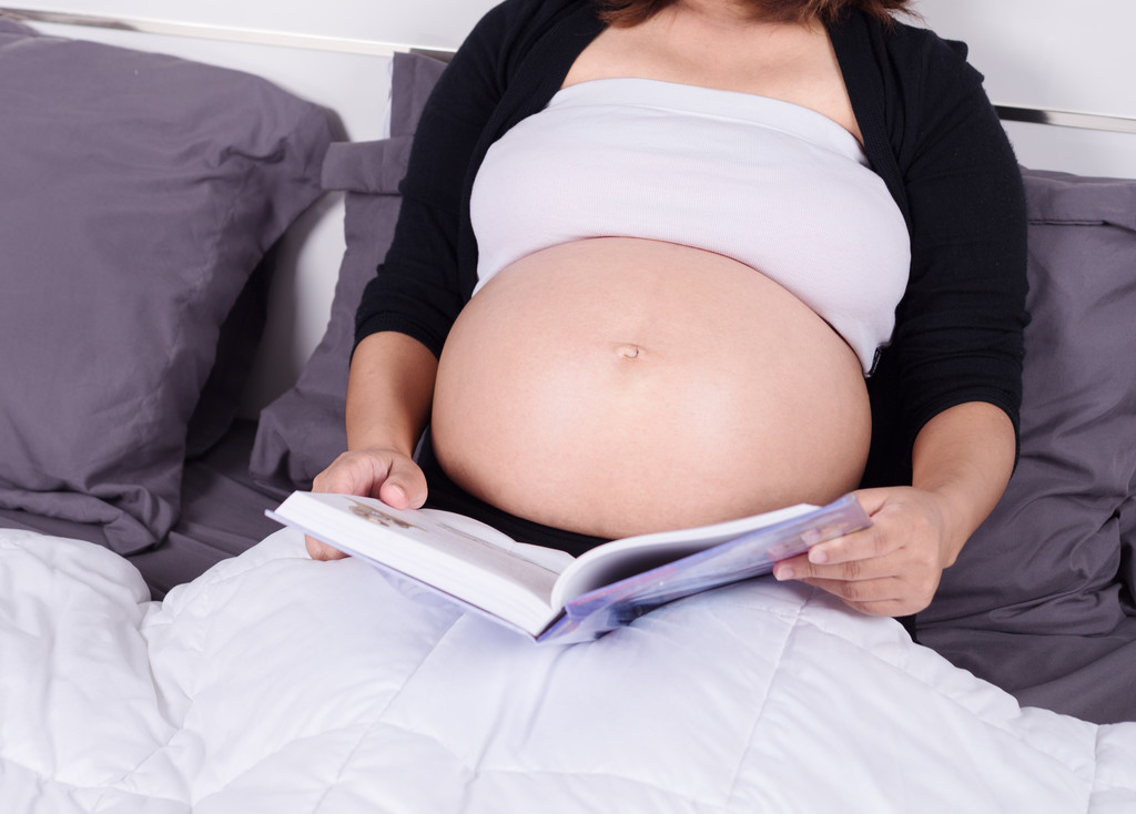 Kobieta w ciąży, czytając książkę leżąc na łóżku w t z bliska - Zdjęcie, obraz