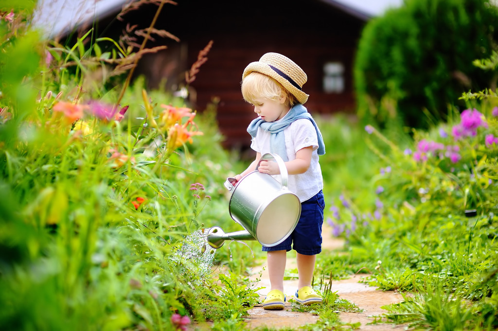 Милий маленький хлопчик в солом'яному капелюсі поливає рослини в саду
 - Фото, зображення