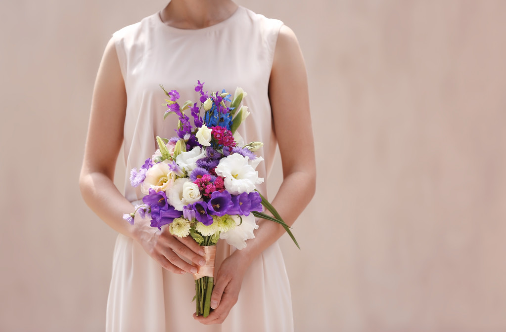 ベージュ色の背景に美しい花の花束を持つ女性 - 写真・画像