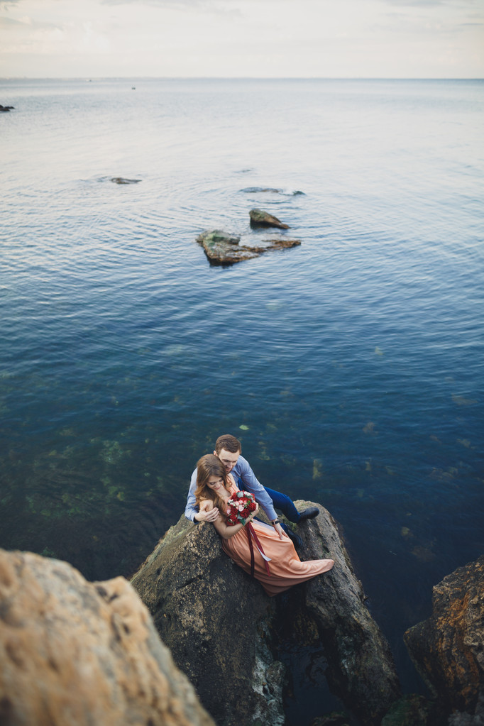 Svatební pár líbání a objímání na skalách v blízkosti modrého moře - Fotografie, Obrázek
