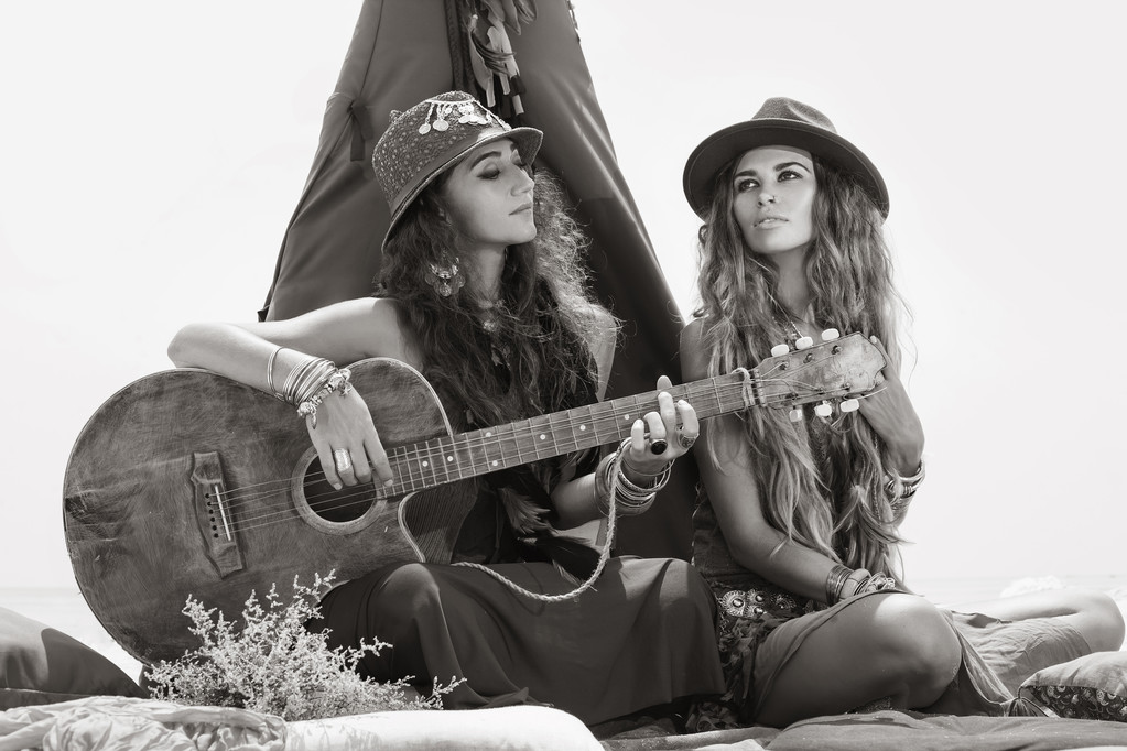 zwei schöne Boho-Mädchen mit Gitarre sitzen auf Kissen am Tipi - Foto, Bild