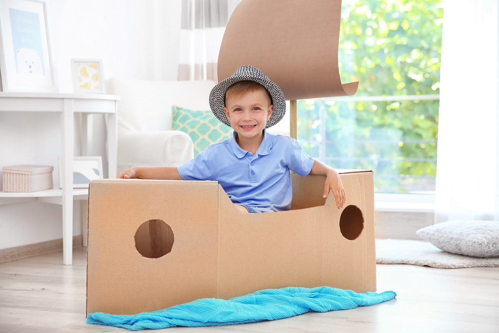 Kleine jongen spelen met kartonnen schip binnenshuis - Foto, afbeelding