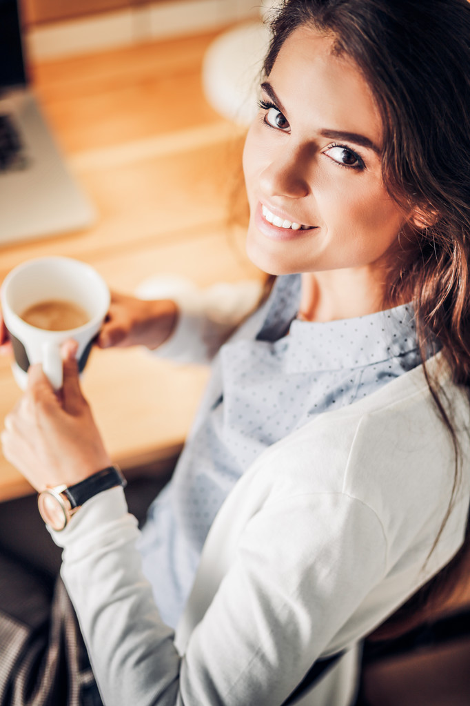 Retrato de una joven relajada sentada en su escritorio sosteniendo una taza de café - Foto, Imagen