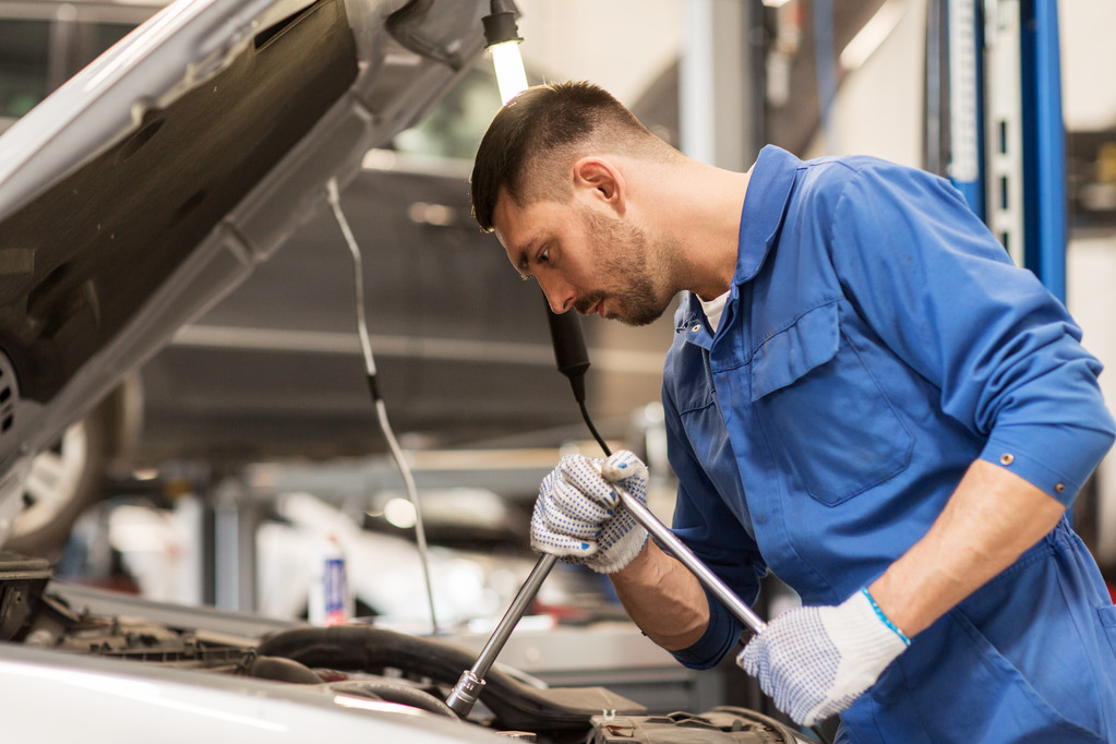 Mechaniker mit Schraubenschlüssel repariert Auto in Werkstatt - Foto, Bild