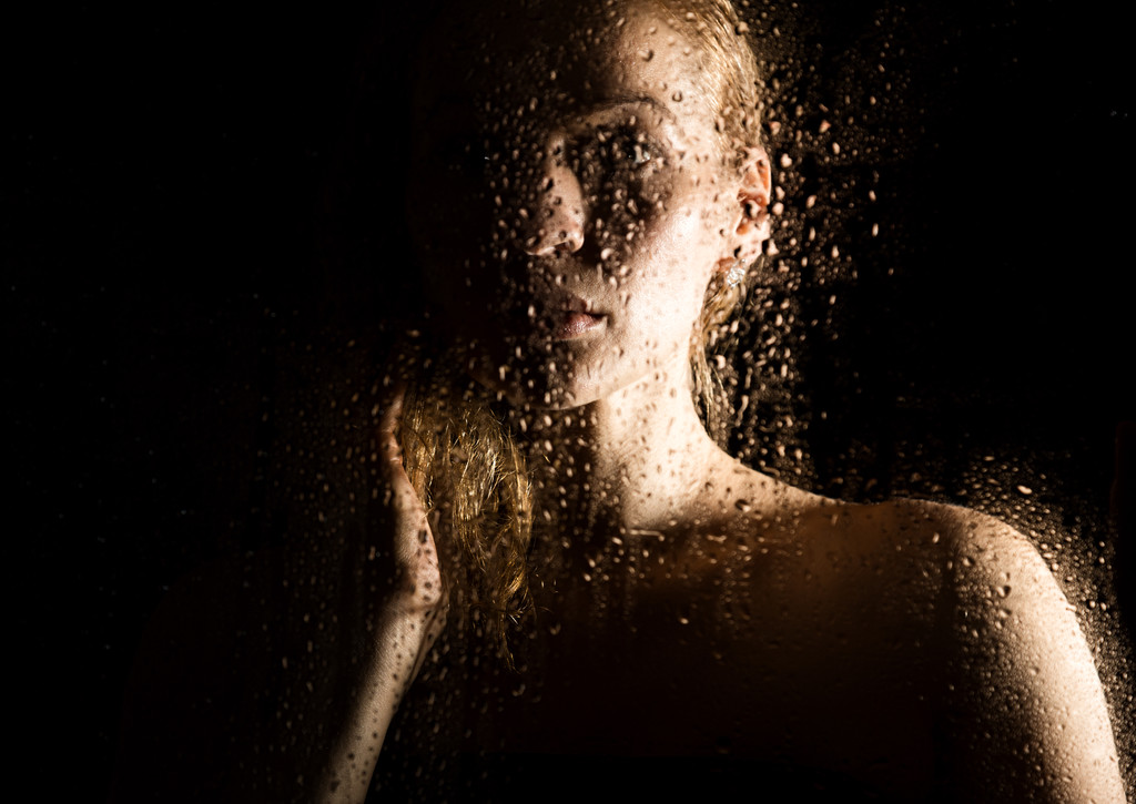 σέξι νεαρή γυναίκα, ποζάρει πίσω από διαφανές γυαλί που καλύπτονται από σταγόνες νερού. μελαγχολική και θλιβερή γυναικεία προσωπογραφία - Φωτογραφία, εικόνα