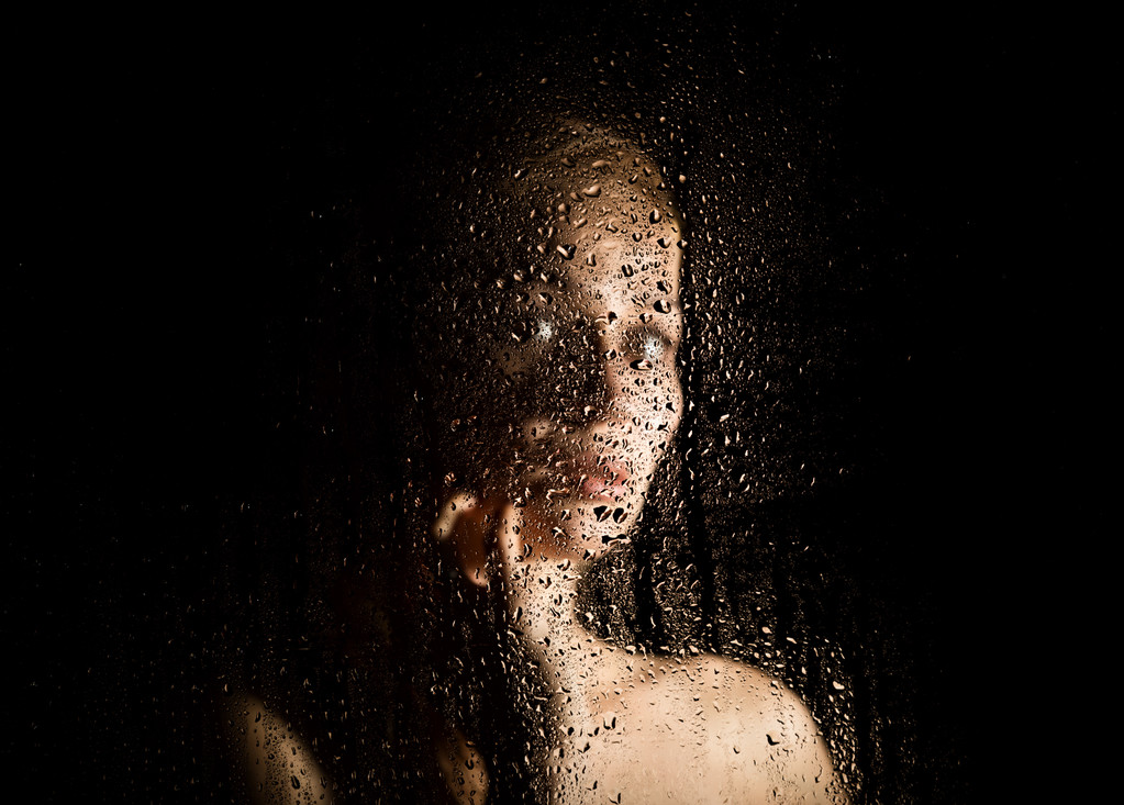 σέξι νεαρή γυναίκα, ποζάρει πίσω από διαφανές γυαλί που καλύπτονται από σταγόνες νερού. μελαγχολική και θλιβερή γυναικεία προσωπογραφία - Φωτογραφία, εικόνα