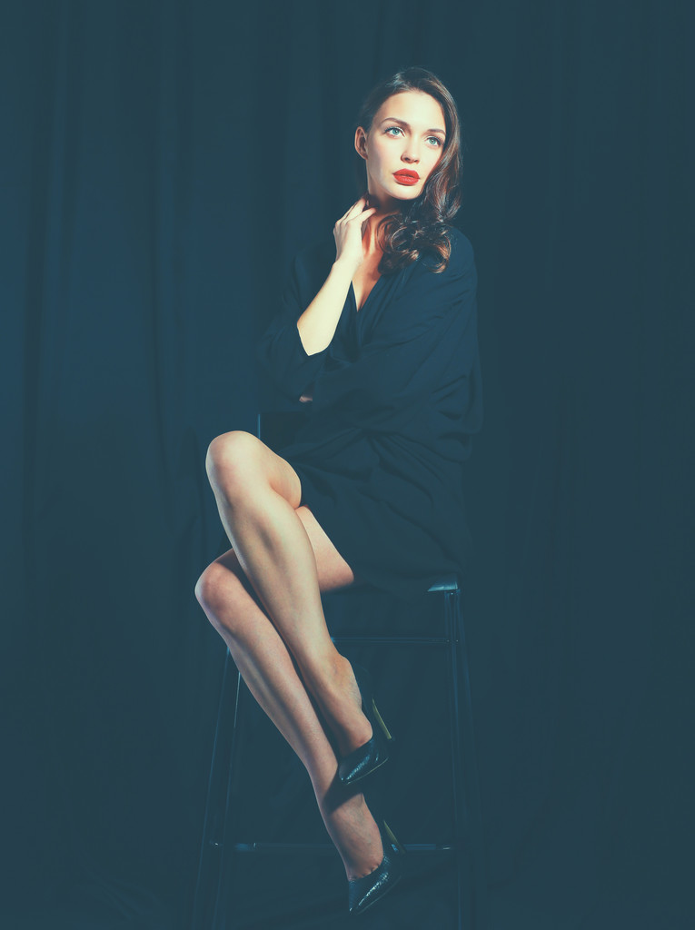 Hermosa mujer sentada en una silla, aislada sobre fondo negro
 - Foto, Imagen