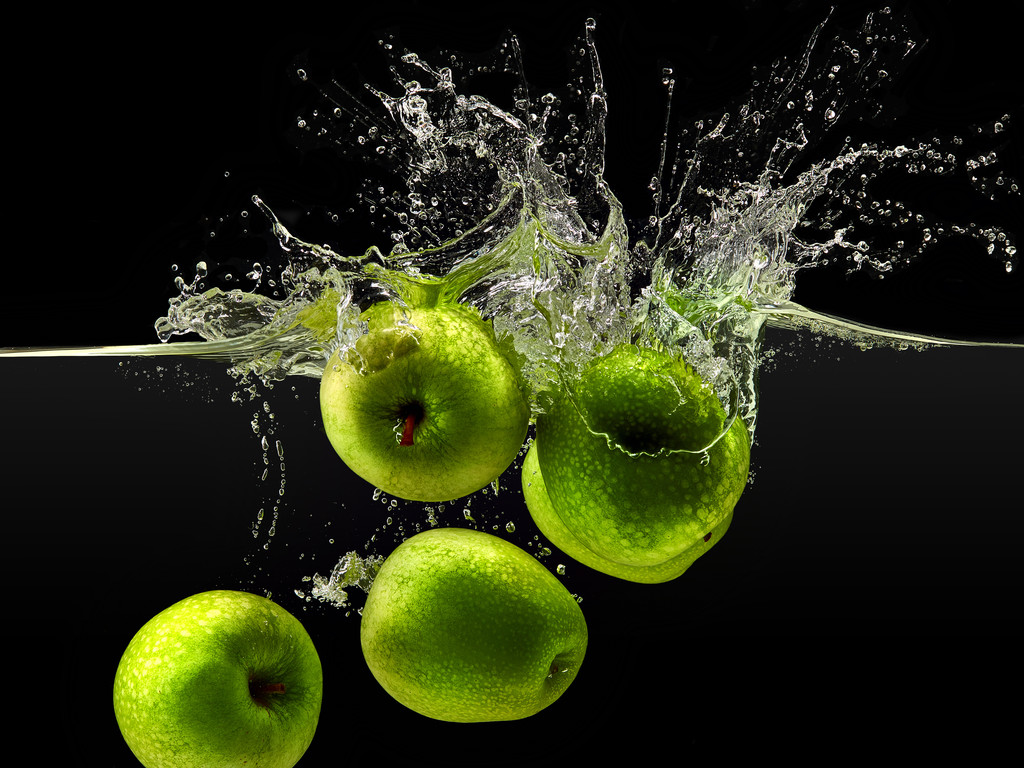 Группа зеленых яблок, падающих в воду на черном
 - Фото, изображение