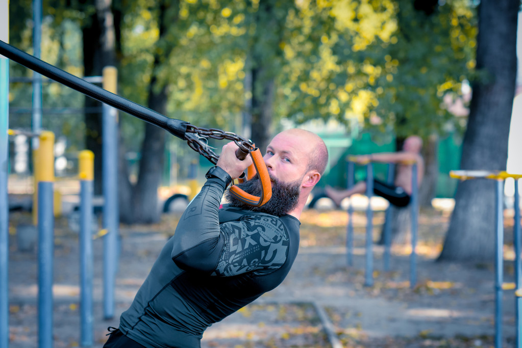 Мускулистый бородатый человек тренируется с ремнями
 - Фото, изображение