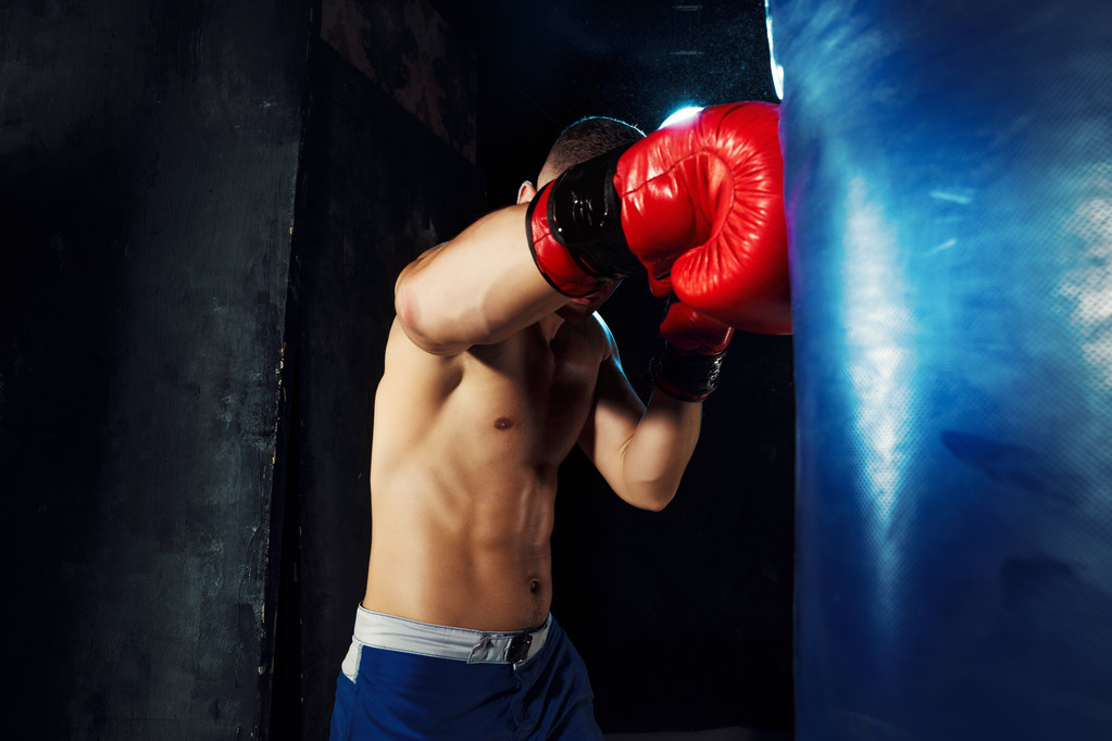 Boxer boxt in Boxsack mit dramatischer, kantiger Beleuchtung in einem dunklen Studio - Foto, Bild