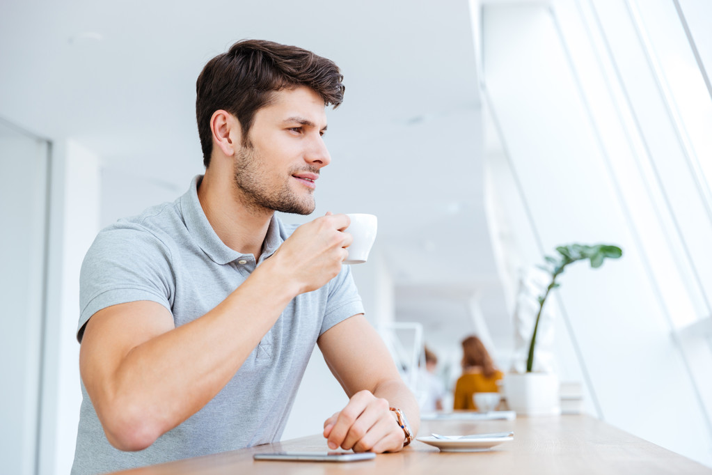 Усміхнений випадковий молодий чоловік п'є каву в кафе
 - Фото, зображення