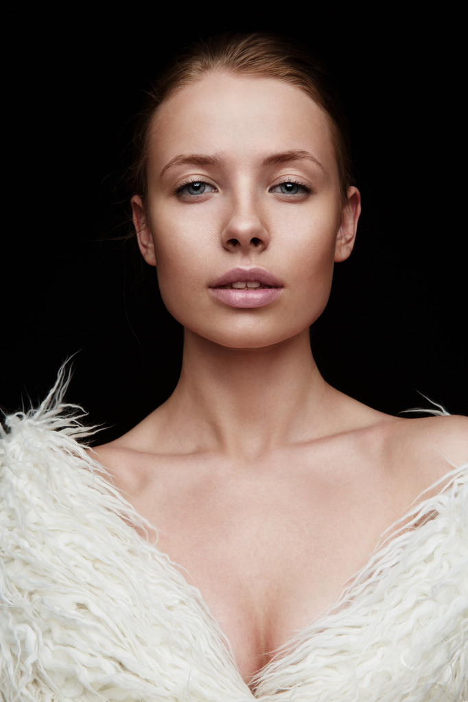 Portrait of a sensual beautiful woman with full open lips and nude makeup on her perfect glowing skin wearing fashionable white artificial fur coat on the naked body is posing in the studio - 写真・画像