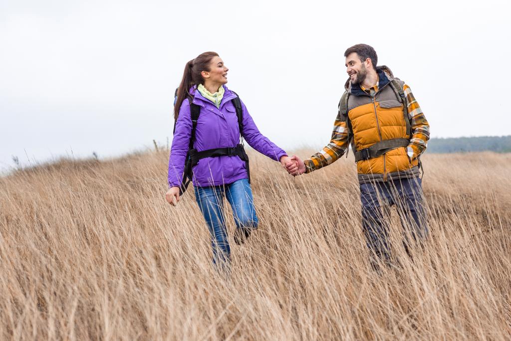 Smiling couple with backpacks walking in grass  - Photo, Image