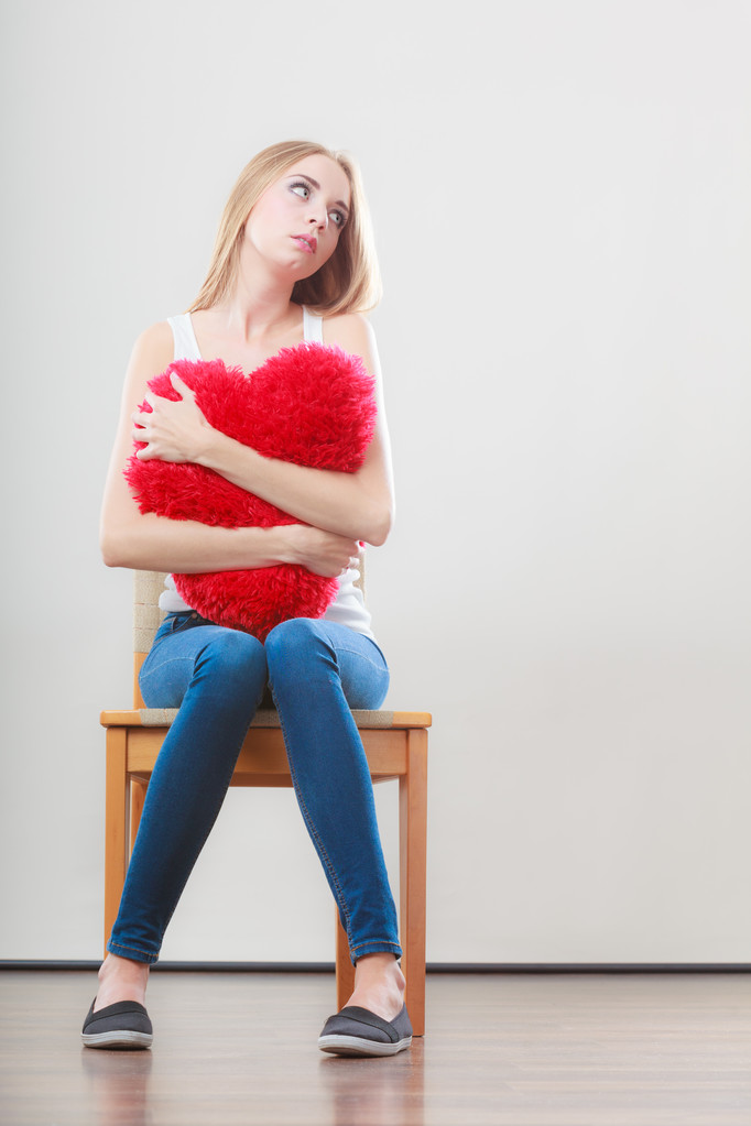 Triste mujer infeliz sosteniendo almohada roja del corazón
 - Foto, imagen