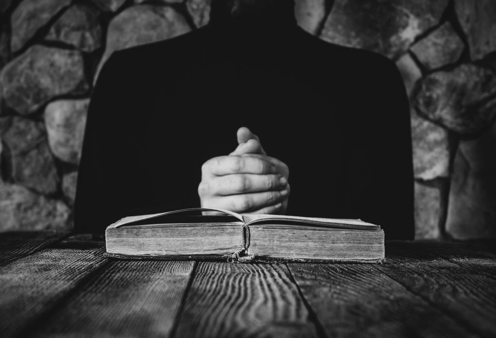 eski açık bir kitap önünde siyah giysili erkek. dua, çalışma, büyücülük kavramı. seçici odak, siyah ve beyaz fotoğraf - Fotoğraf, Görsel