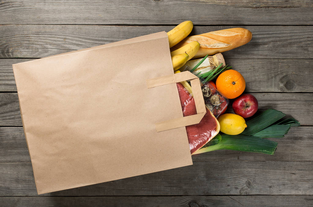 Různé potraviny v papírové tašce na dřevěné pozadí, zblízka - Fotografie, Obrázek