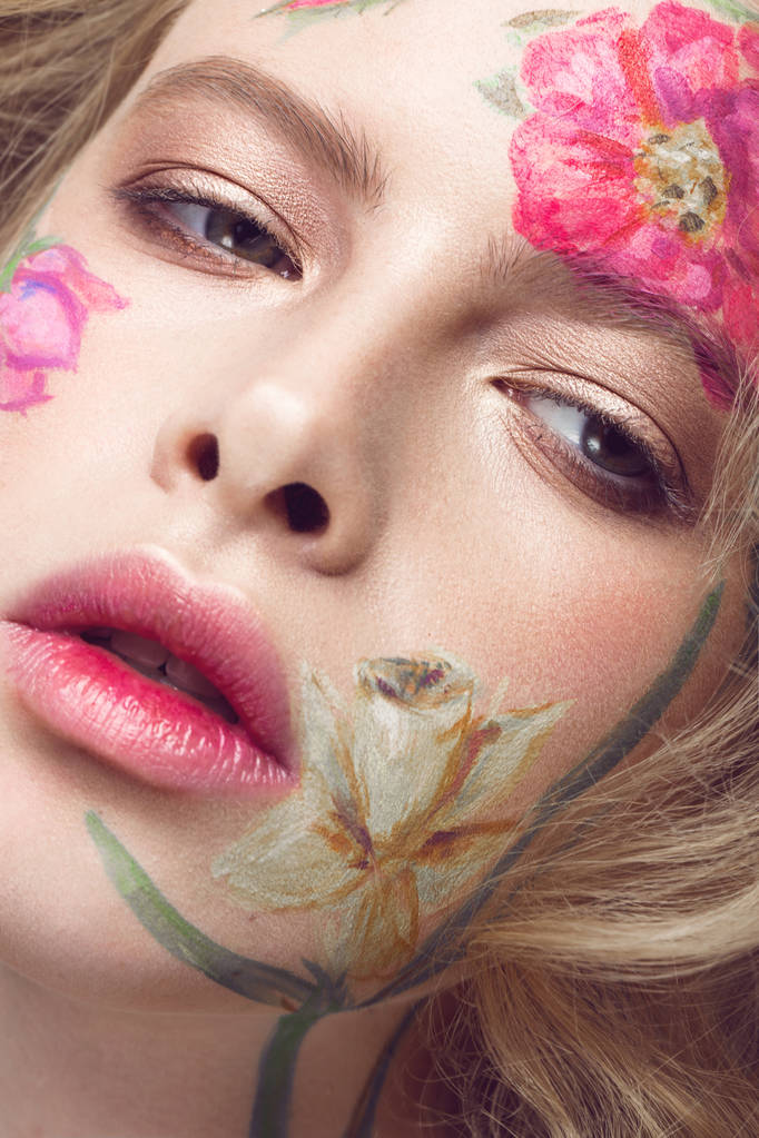 Belle fille blonde avec des boucles et un motif floral sur le visage. Fleurs de beauté
. - Photo, image