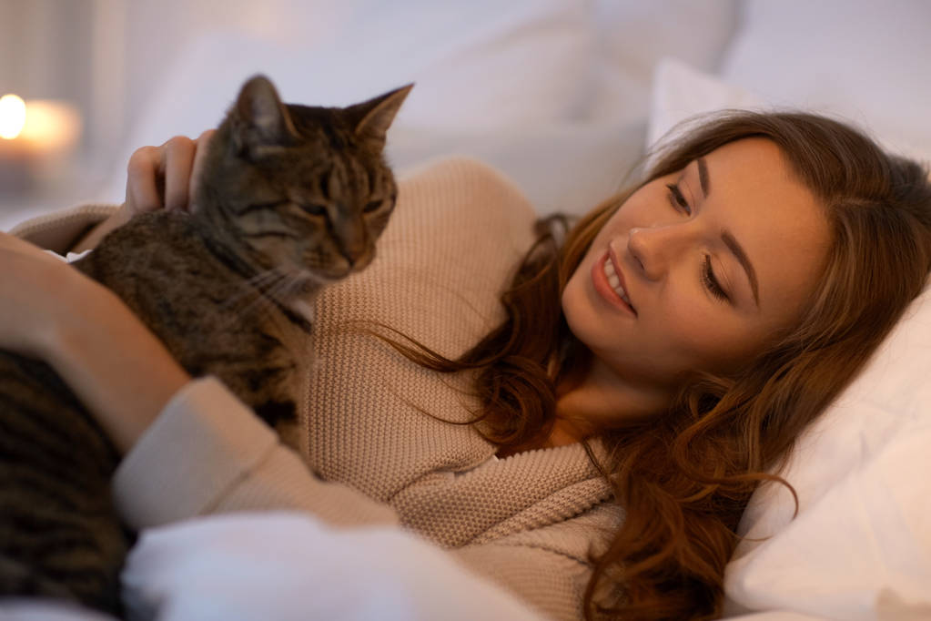 feliz joven con gato acostado en la cama en casa
 - Foto, imagen