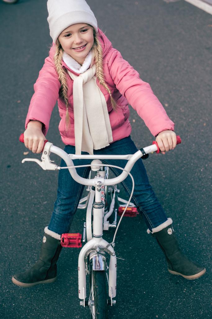 Αξιολάτρευτο χαμογελαστό κορίτσι που κάθεται στο ποδήλατο - Φωτογραφία, εικόνα